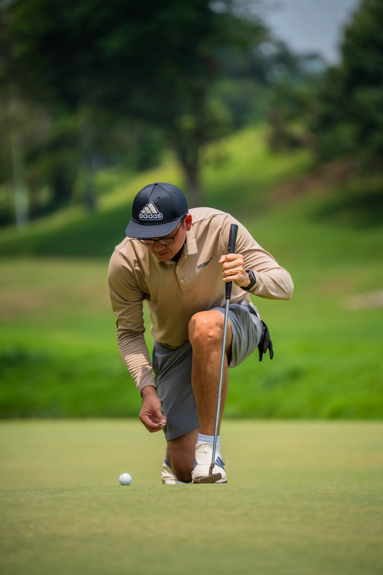 Portrait-style action photo of a golfer crouching on a green while lining up a putt during a golf event.